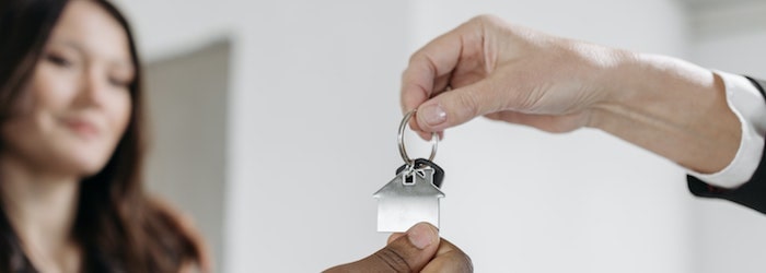 Deux mains tenant un porte-clé maison avec une femme souriant en arrière-plan